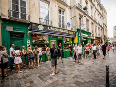 many people are standing in line to buy food at the street side store on a cobblestone sidewalk