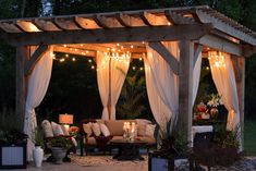 an outdoor living area with white curtains and lights