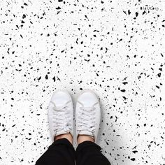 someone's feet in white sneakers standing on a speckled floor