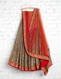 a red and gold lehenga hanging on a white brick wall in front of a brick wall