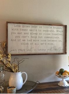 a wooden sign hanging on the wall above a table with flowers and fruit in vases