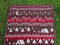 a crocheted rug with trees and mountains on it in the grass, next to a pair of scissors