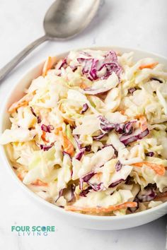 a white bowl filled with coleslaw and carrots next to a silver spoon