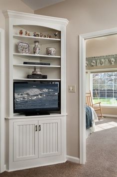 a living room with a large tv on top of a white entertainment center next to a window