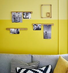 a living room with yellow walls and pictures hanging on the wall above the gray couch