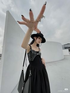 a woman in black dress and hat holding up her hand