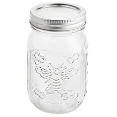 a glass jar with a metal lid and a bee design on the front, sitting on a white background