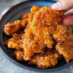 a hand is picking up some chicken wings from a black plate with sesame seeds on top