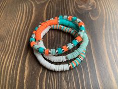 three bracelets with different colored beads on top of a wooden table next to an orange, white and blue bead