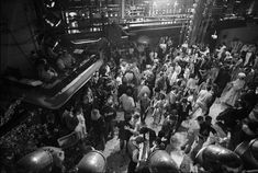 black and white photograph of people in an industrial area with helmets on their heads, looking down at the floor