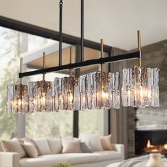 a chandelier hanging over a living room table with couches and fireplace in the background