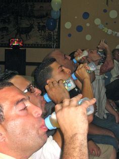 the man is drinking from his bottle while another person takes a photo with his cell phone