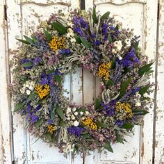 a wreath is hanging on an old door with purple, yellow and white flowers in it