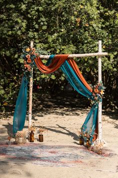 an outdoor wedding setup with orange and blue draping on the ground, decorated with flowers