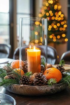 a candle and some pine cones are sitting on a table with an orange in the center