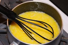 a metal pot filled with yellow liquid and whisk on top of a stove