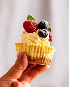 a hand holding a small cupcake with berries and cream frosting on the top