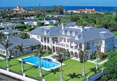 an aerial view of a large mansion with a swimming pool in the foreground and palm trees surrounding it