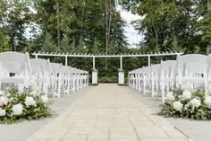 an outdoor ceremony setup with white chairs and flowers on the aisle, surrounded by greenery