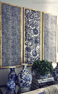 three blue and white vases sitting on top of a table next to two paintings