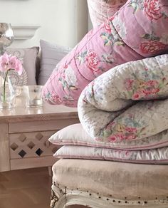 the pillows are piled on top of each other near a table with flowers in it