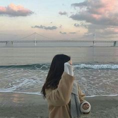 a woman sitting on the beach looking out at the ocean with her hand up to her face