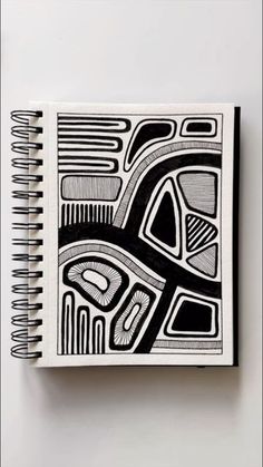 a black and white drawing on top of a spiral notebook with an abstract design in the middle