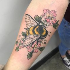 a tattoo on the arm of a person with a bee and flowers tattooed on it