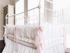 a white crib with pink bows on the bottom and side rails, next to a window