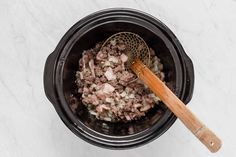 a wooden spoon in a black crock pot filled with ground beef and onions on a white marble surface