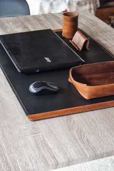 a desk with a laptop, mouse and leather tray on top of it next to a cup