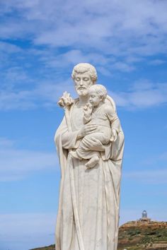 a statue of jesus holding a child on top of a hill in front of a blue sky