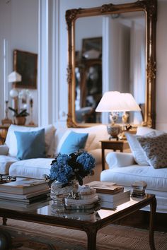 a living room filled with white couches and blue flowers on top of a coffee table