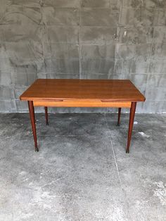 a small wooden table sitting on top of a cement floor next to a brick wall