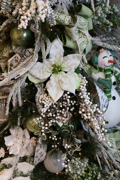 a christmas tree decorated with white flowers and green leaves, snowman ornament