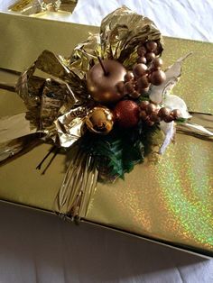 a wrapped present with gold foil and ornaments on it's side, sitting on a white table cloth