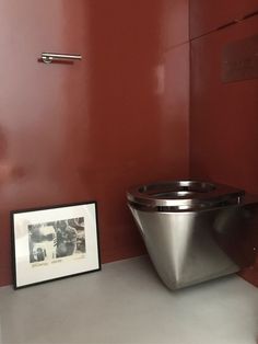 a silver toilet sitting next to a red wall in a bathroom with a picture frame