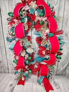 a christmas wreath with red bows and ornaments on the front, against a white wooden background