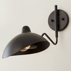 a black wall light mounted on the side of a white wall next to a lamp