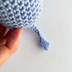 a crocheted blue object being held up by someone's hand on a white surface