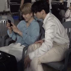 two people sitting next to each other in chairs looking at their cell phones and smiling