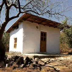 a small white building sitting on top of a dirt hill next to a tree and rocks