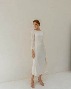 a woman standing in front of a white wall wearing a dress with long sleeves and an asymmetrical neckline