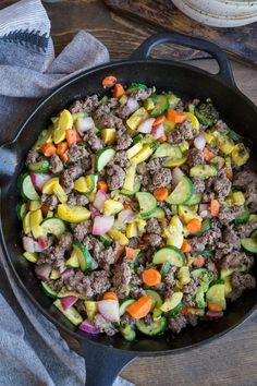 a skillet filled with meat and vegetables on top of a wooden table