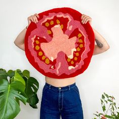 a woman holding up a large red rug with an image of a flower on it