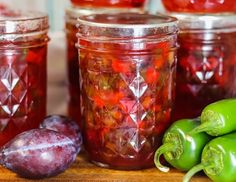 several jars filled with pickles and peppers on a wooden table next to green peppers