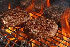 hamburger patties cooking on the grill with flames