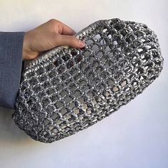 a hand holding a silver purse on top of a white table