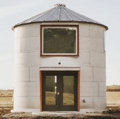 a round building with two doors and a window on the top floor in an open field