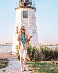 a woman standing in front of a light house with her hand up to the side